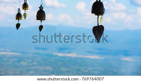 Many bells are hung by the backdrop of a wide natural landscape, and the clear sky during the daytime.