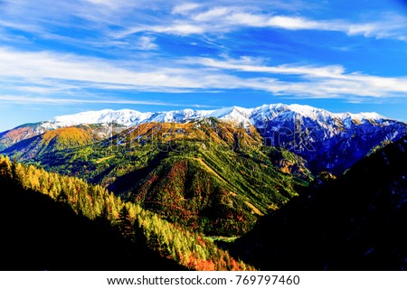 unique panorama landscape in the austrian alps pictured in autumn with multiple colours from the green valley, yellow and red dotted forrest and a white mountain ridge next to the peaks