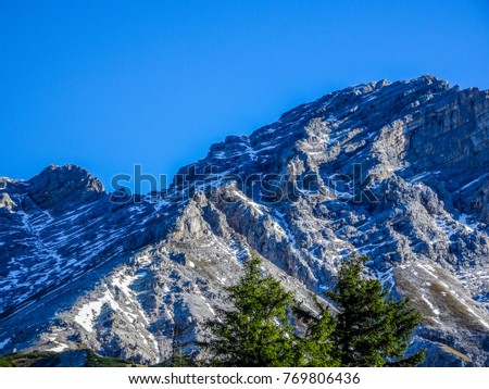 Spectacular mountain view in the austrian alps with a ridge dividing the picture in a light and a dark side, all covered with pieces of snow and two tree tops in front