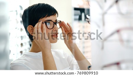 health care, eyesight and vision concept - happy woman choosing glasses at optics store Royalty-Free Stock Photo #769809910