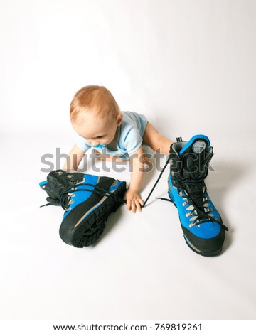 little boy sitting near a mountaineering boots on a white background