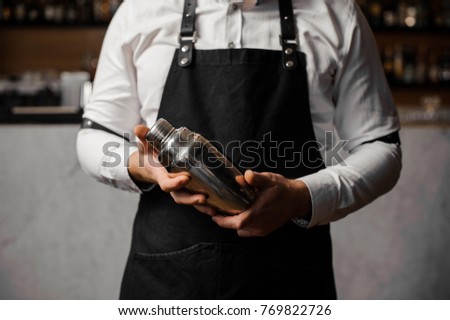 Barman`s hands holding a professional shaker against the blurred indoors background of the bar counter Royalty-Free Stock Photo #769822726