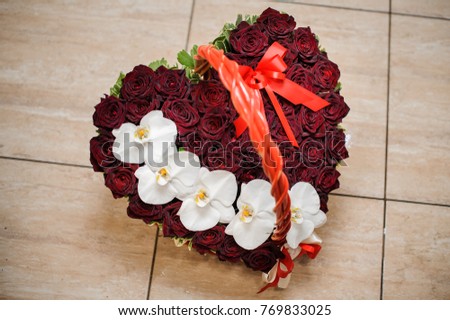 Elegant heart-shaped box with a flower composition of pink roses decorated with a red bow for Valentine`s day