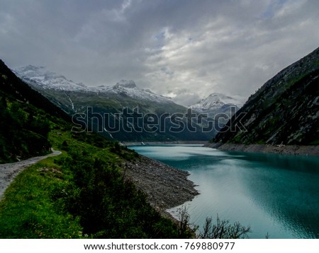 Artificial high alpine mountain lake in the austrian alp region tyrol in the valley zillertal on a very cloudy day with high mountains in the background panorama covered with snow and ice