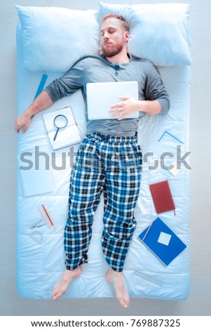 Going to work. Relaxed male person holding laptop on the belly and keeping eyes closed while lying on cozy blanket