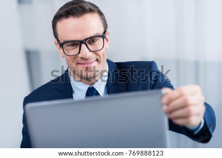 Online communication. Merry positive brunette man touching screen while staring at it and smiling 