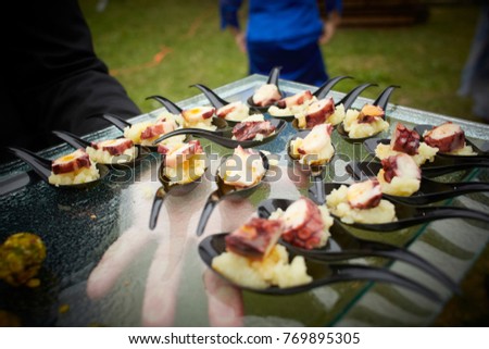 Waiter serving appetizers. Spoons with octopus food and smashed potatoes. Close up picture