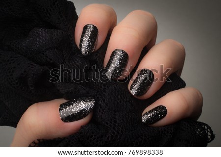 Female hand with black nails and silver glitters is holding black textile on gray background.