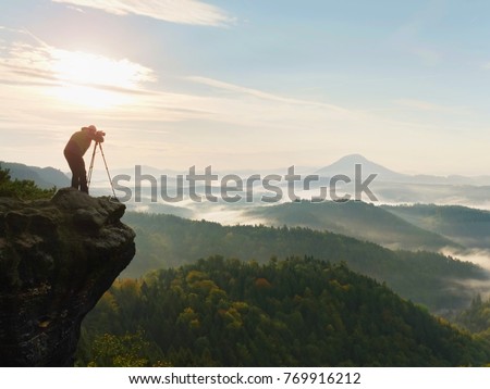 Nature photographer in the action.  Man silhouette above a misty clouds,  morning hilly landscape.