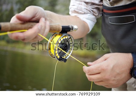 Fly fisherman using a spinning reel with yellow line in a close up view on his hands against water with green reflections Royalty-Free Stock Photo #769929109