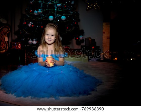 A little girl in a dark room, on Christmas night, with a burning candle in her hands. Concept of a holiday, Christmas, family well-being, Happy childhood. 
