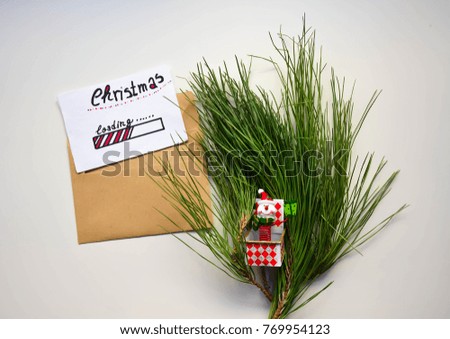 An envelope with Christmas loading text on a note and green tree branch on white wooden table