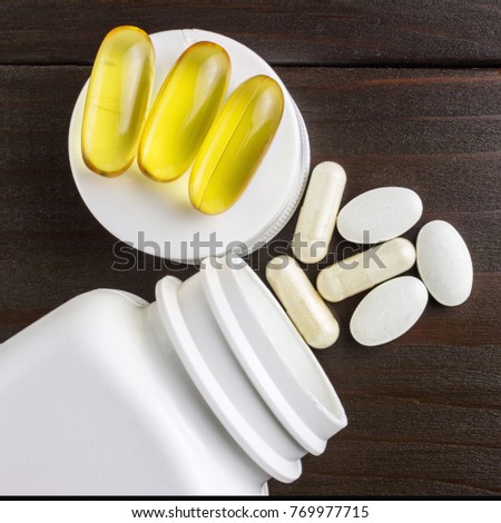Complex of vitamins and dietary supplement, yellow capsules omega 3, white of glucosamine, calcium pills, white plastic bottle on wooden table, top view.