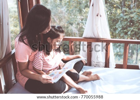 Happy family asian mother and daughter read a book together in the room in vintage color tone