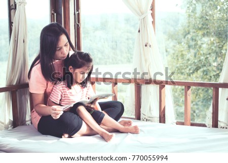 Happy family asian mother and daughter read a book together in the room in vintage color tone