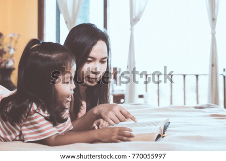 Happy family asian mother and daughter read a book together in the bedroom in vintage color tone