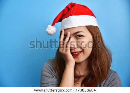 Portrait of Asian female and Santa Claus hat smiling and holding her face with her hand on Blue background. Christmas and New year concept. Happy. Fashion.