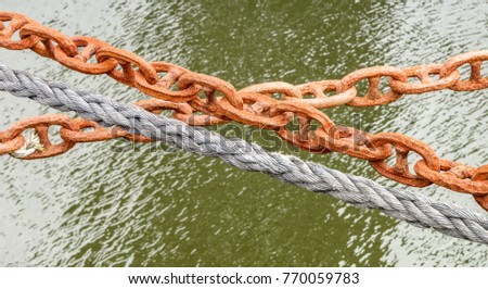 Ship docking chain and rope line close-up perspective over rippled surface of harbor waters.