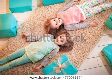 Two sisters twins for the New Year and Christmas lie on the floor among many gift boxes. The girls in their pajamas smile beautifully.