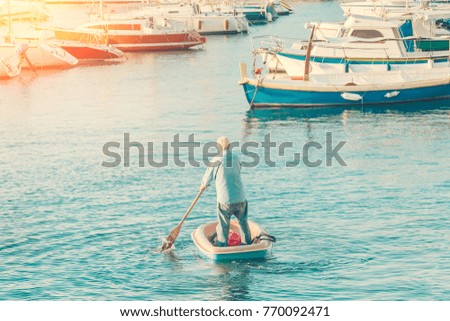 Old man sailing on a small rowing boat to the yacht berth in the sunlight