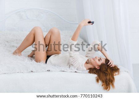 A girl lies on a bed with a smile and does selfie on a white background
