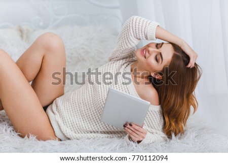 Girl with a tablet in her hand lies on a bed and straightens her hair close-up on a white background