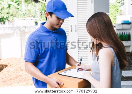 Woman putting signature in clipboard on cardboard box with delivery man