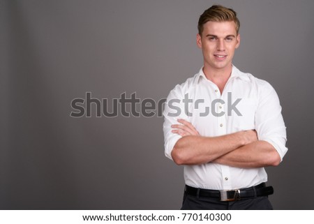 Studio shot of young handsome businessman with blond hair against gray background