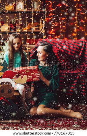 Portrait of brunette mom and little daugther wearing in green dresses giving presents each other for x mas and new year holidays. Happy family of mother with pretty girl celebrating Christmas.