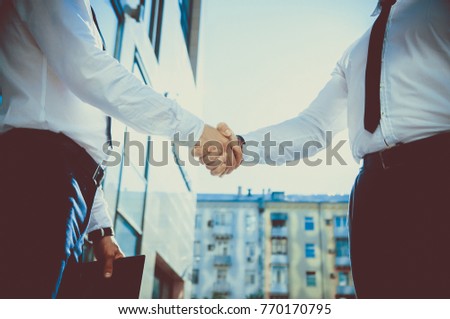 Handshake of two young men against a multi-storey office building. Make a deal. Friendly relations. Office staff. Signing of the contract.