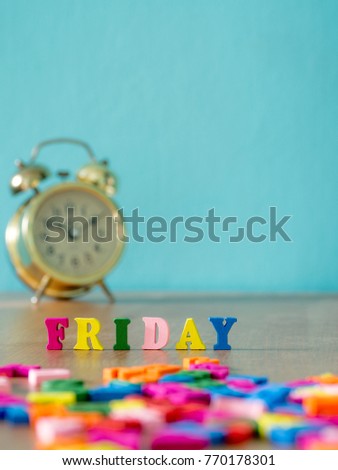 Colorful wooden word FRIDAY on wooden table and vintage alarm clock and background is powder blue. English alphabet made of wooden letter color.