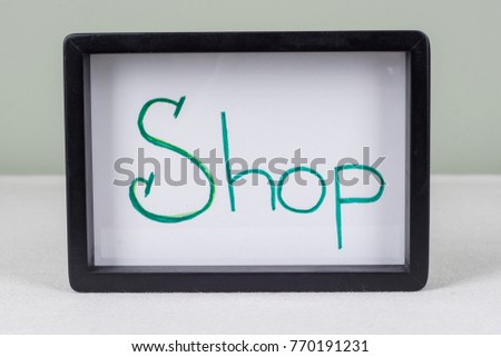 Text word SHOP, in black frame, on white table.