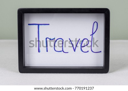 Text word TRAVEL, in black frame, on white table.