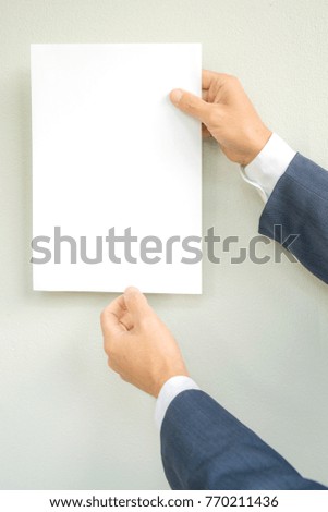 Man hand holding white paper A4 size on gray background,mock up style,business concept.