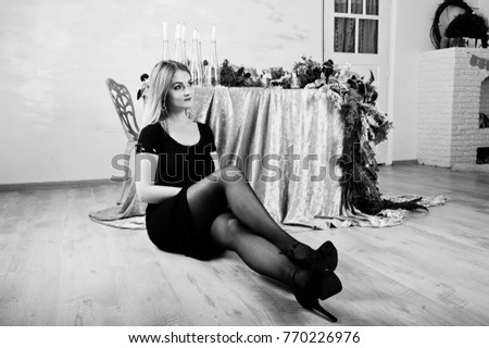 Blonde girl in black dress posed near table with christmas candles decor in white room.