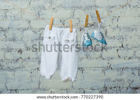 Children's shoes and pantyhose dry on a rope against a white brick wall.