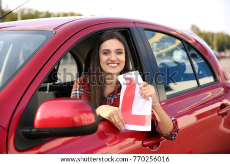 Happy young woman holding learner driver sign in car