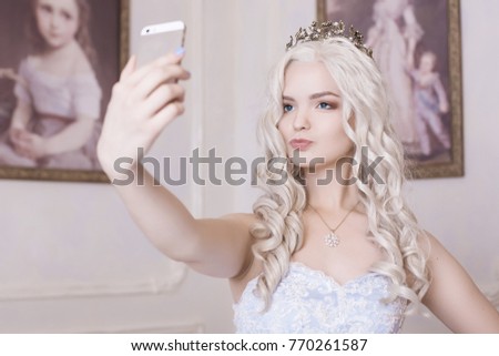 A glamorous girl, a blond woman in a crown, makes a selfie. Spoiled girl, a daughter of an oligarchy. Photograph on an expensive smartphone, narcissist. Princess on the background of the picture.