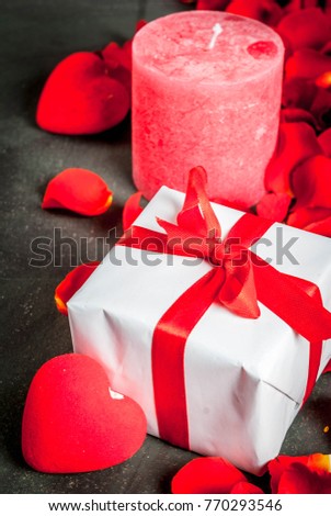 Valentine's day concept, with rose flower petals and white wrapped gift box with red ribbon, on dark stone background, copy space