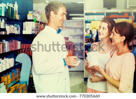 portrait of posiive  man druggist in white coat giving advice to customers in pharmacy