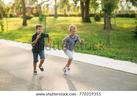 Two children are playing in the park. Two beautiful boys in T-shirts and shorts have fun smiling. They eat ice cream, jump, run. Summer is sunny Royalty-Free Stock Photo #770319355
