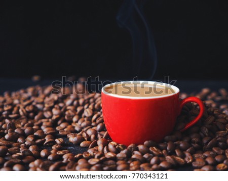 Steaming coffee red cup on roasted coffee beans over bark background.
