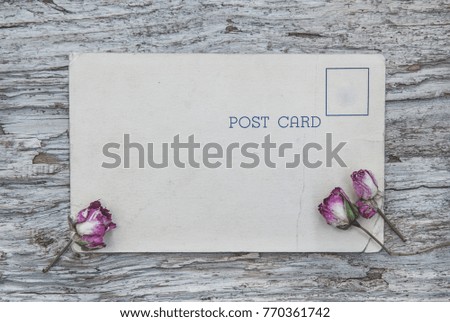Vintage postcard and dry tea roses on the old wooden background