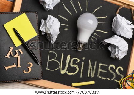 Chalkboard with wrinkled paper, notepad, pen, numerals and lamp. Process of business idea creation. Creasy paper by light bulb with stationery on grey blackboard background. Business idea concept