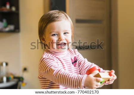Toddler girl playing with her toy photo camera at home, wearing striped turtleneck sweater