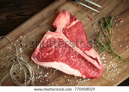 raw t bone steak of beef on the butcher's Board with pepper, salt, herbs, close twine, top view Royalty-Free Stock Photo #770408029