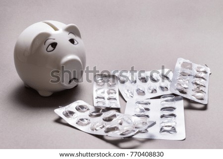 Sad piggy bank, not enough money for Medical tablet on grey back