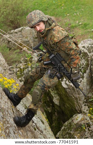 Ukrainian soldier climbing the rock on a rope. Military man in heavy combat ammunition climbs the mountain Royalty-Free Stock Photo #77041591