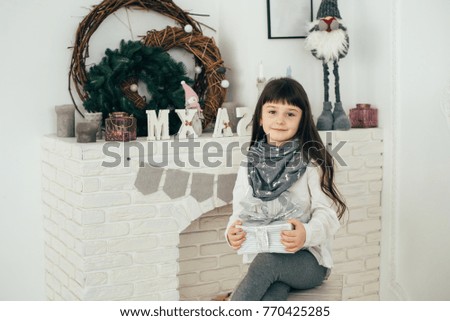 A girl sits at the fireplace and holds a box with a gift in her hands