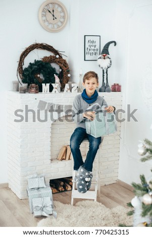 The guy schoolboy sits at the fireplace and holds the box with a gift in his hands